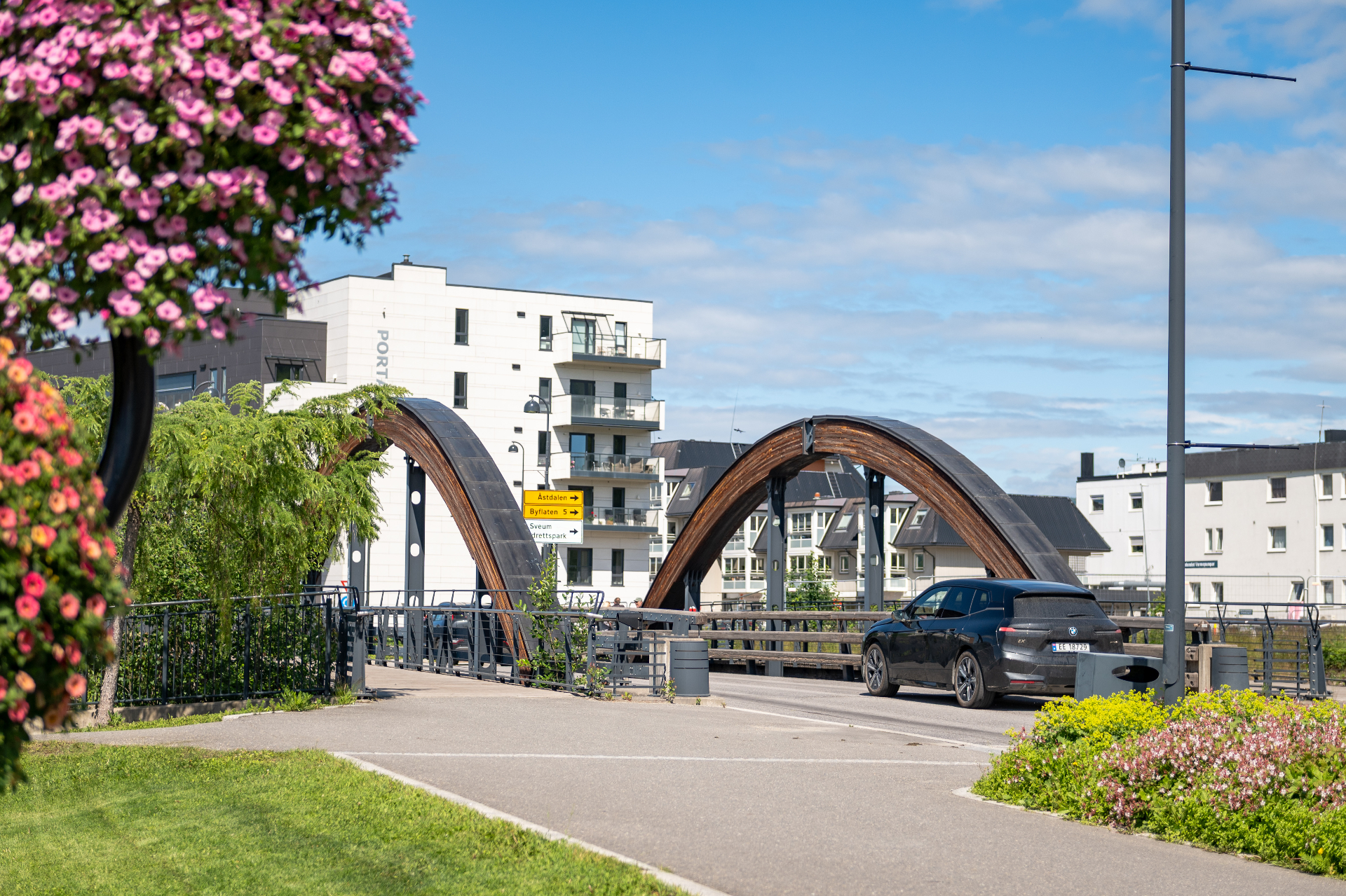 Trebroen i Brumunddal sentrum med sommerblomster og leiligheter i bakgrunnen